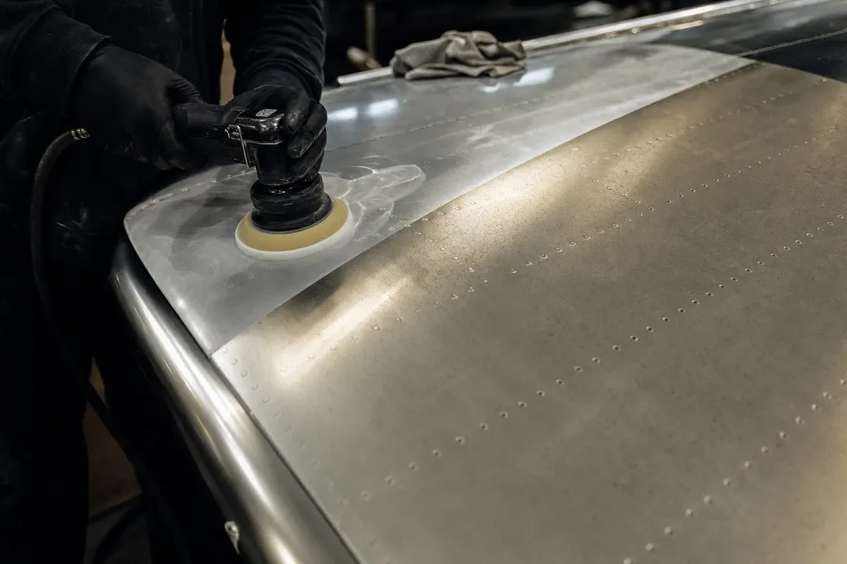 A foam pad refining a brightwork panel, hazed half against duller unworked metal
