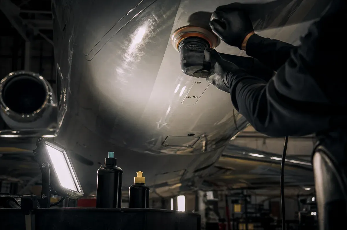 A polisher correcting a painted jet belly panel under raking work light