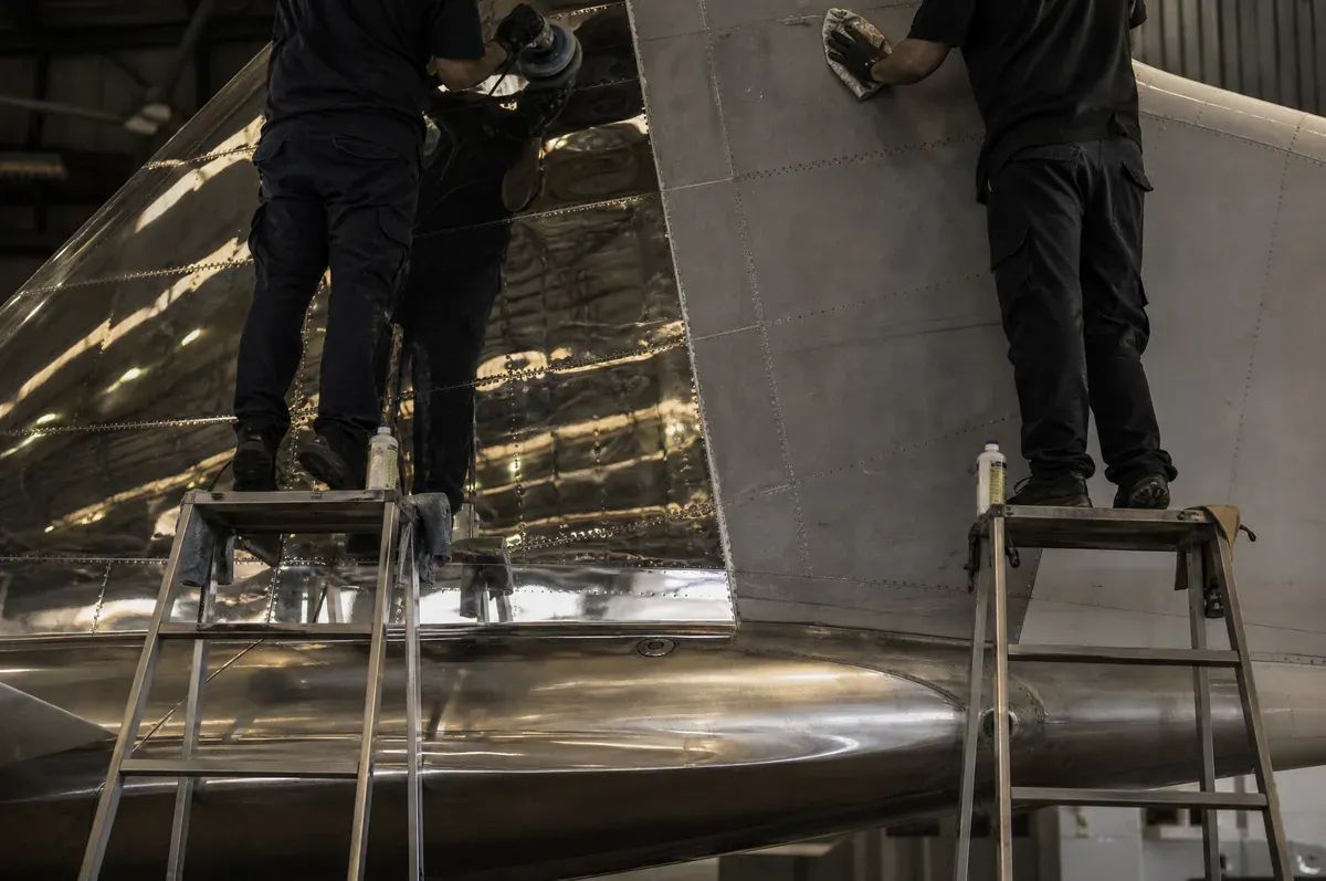 Two technicians on ladders working adjacent panels on a jet tail