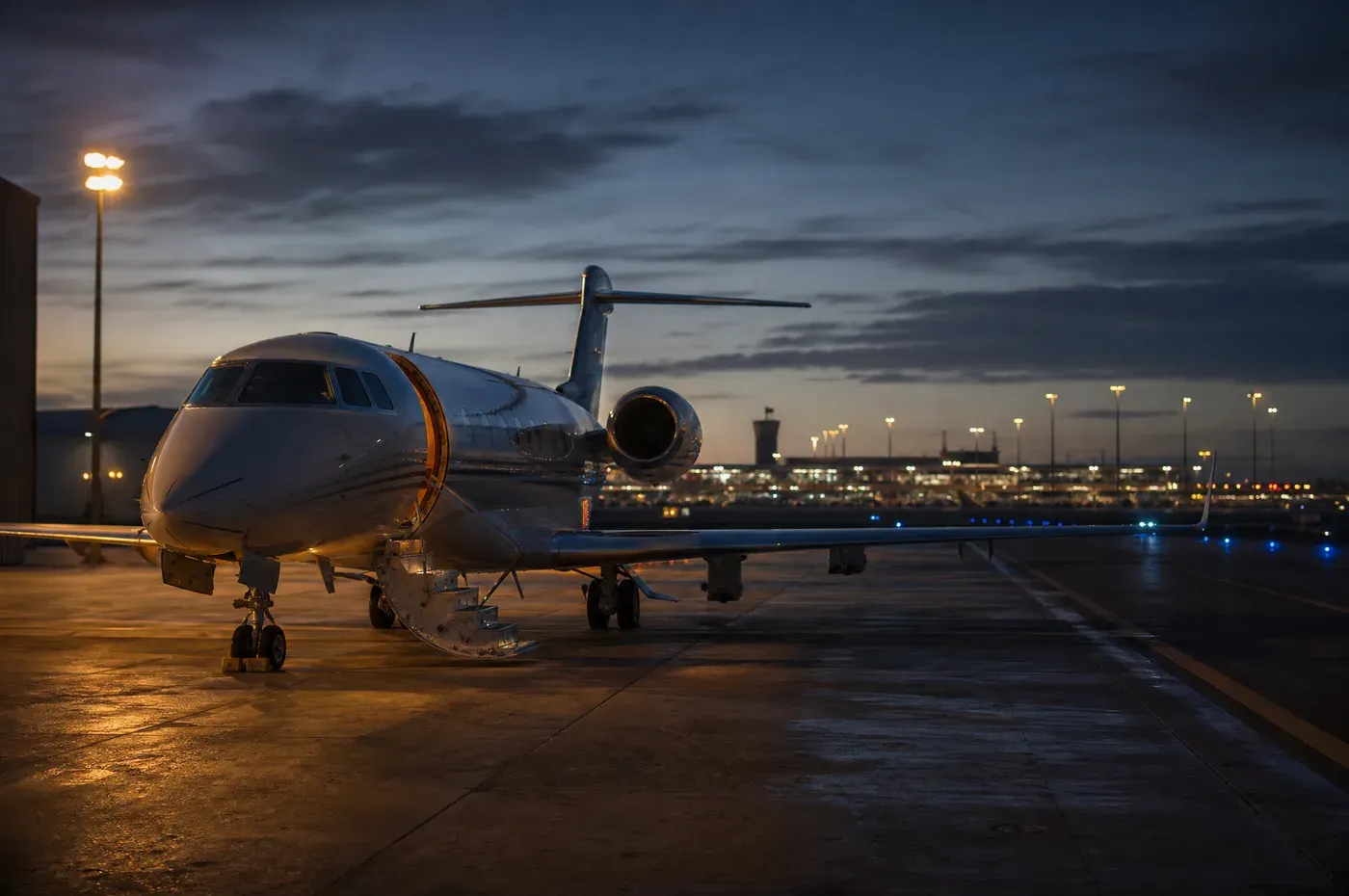 A business jet at dusk with the commercial terminal lit in the distance