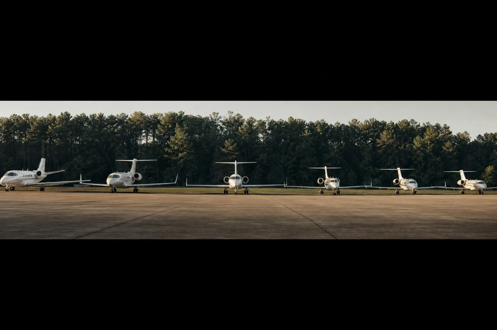 A corporate FBO apron with jets in a precise row against a treeline