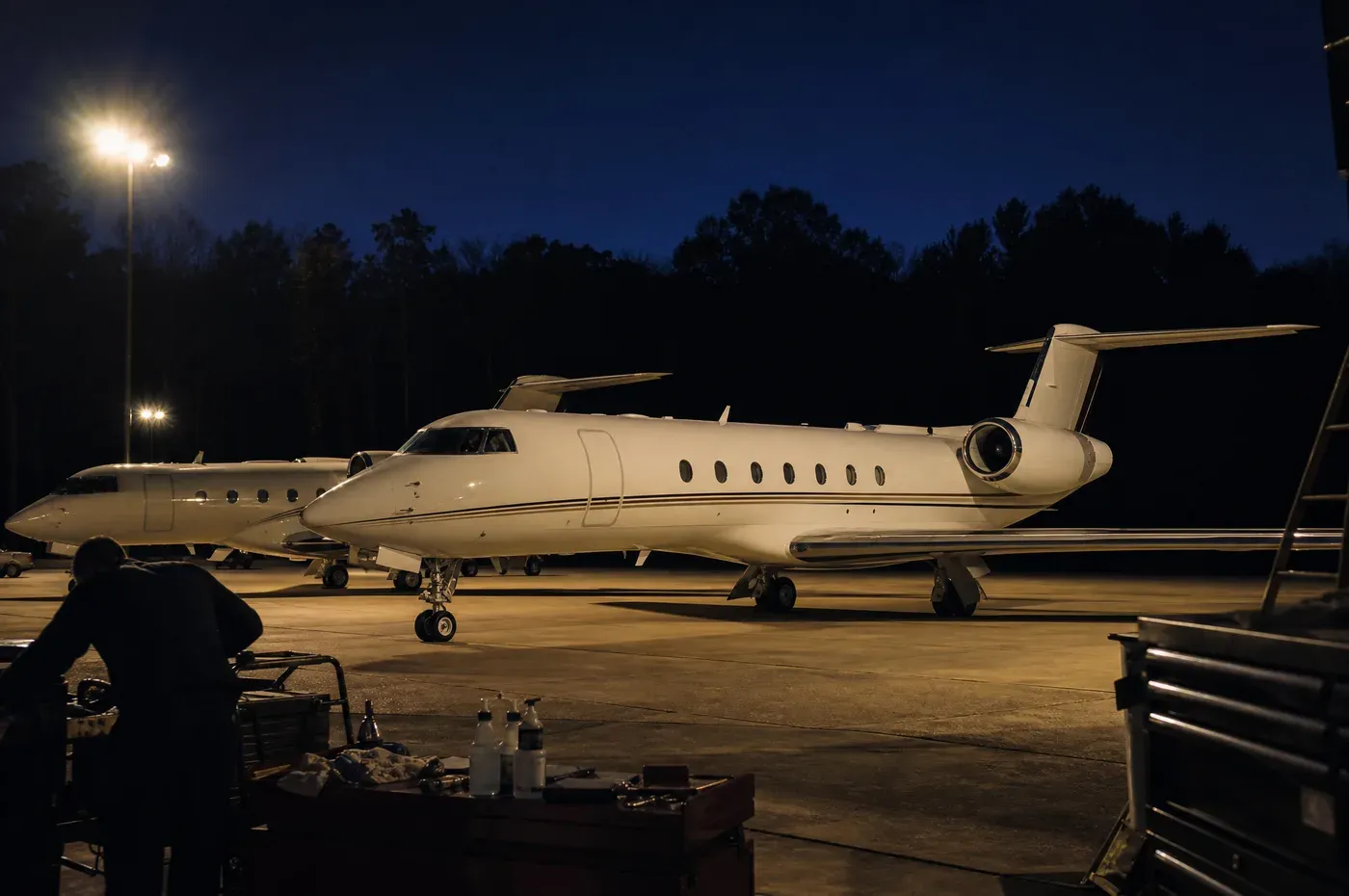 Two jets on a corporate ramp at late dusk against a dark treeline