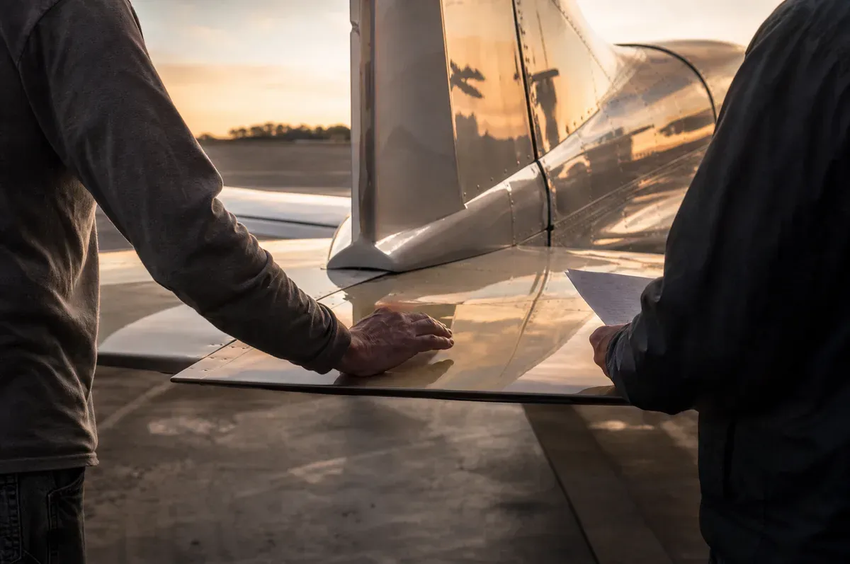 Two people at the tail of a finished light aircraft at the end of the day