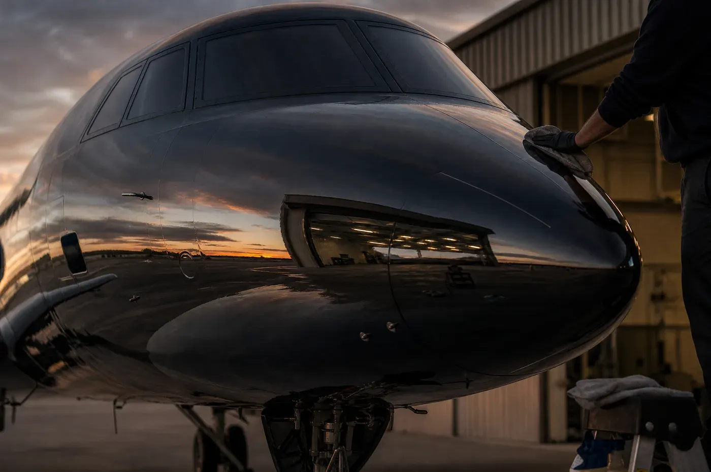 The polished forward fuselage of a business jet mirroring the ramp at dusk