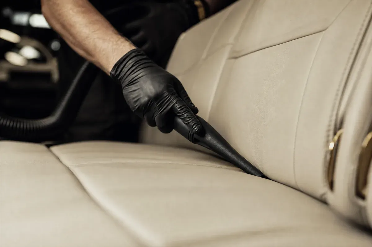 A crevice vacuum tool drawn along the seam of a cream leather cabin seat