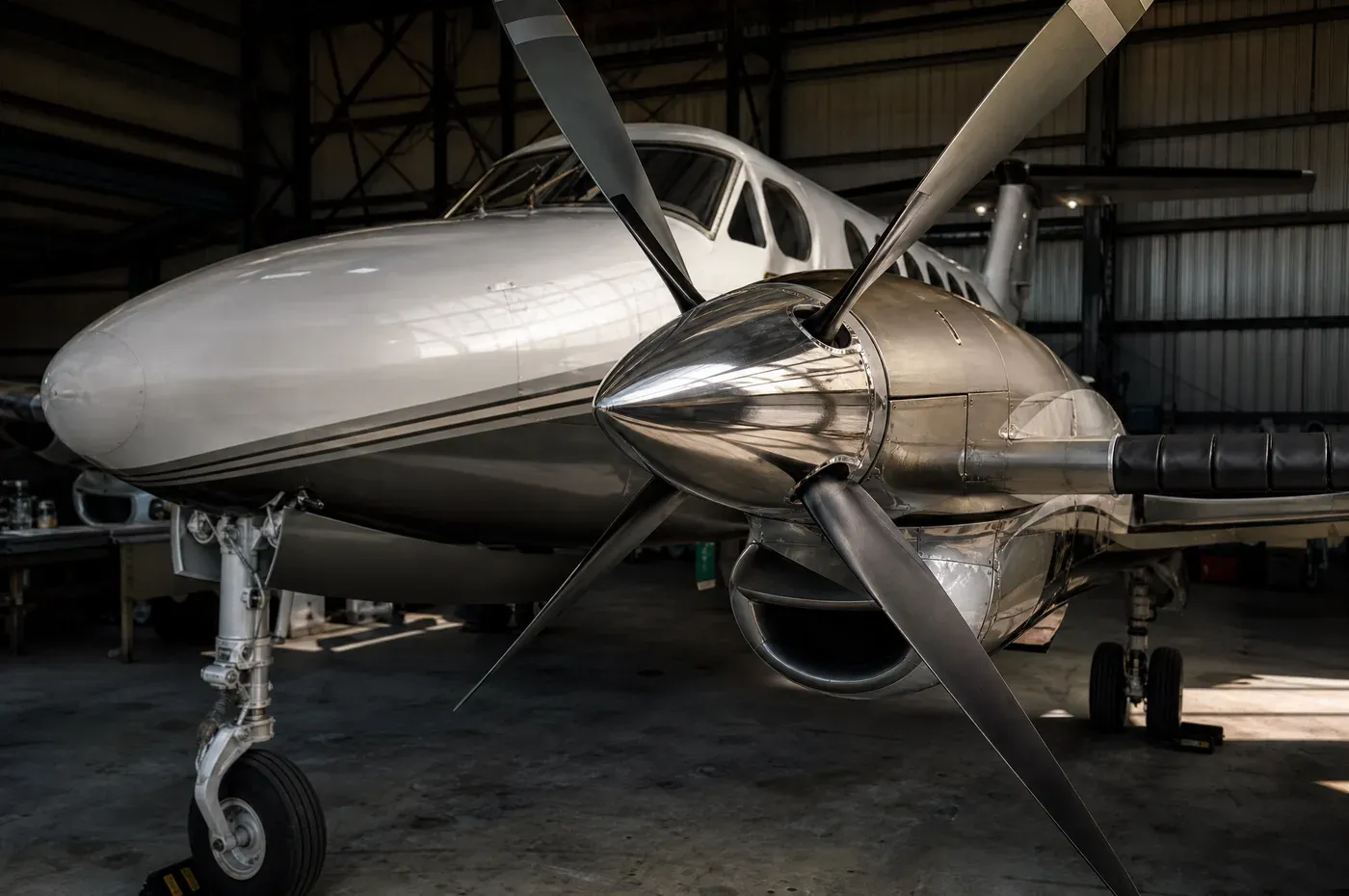 A twin turboprop in a hangar showing polished spinner, propeller and wing boots